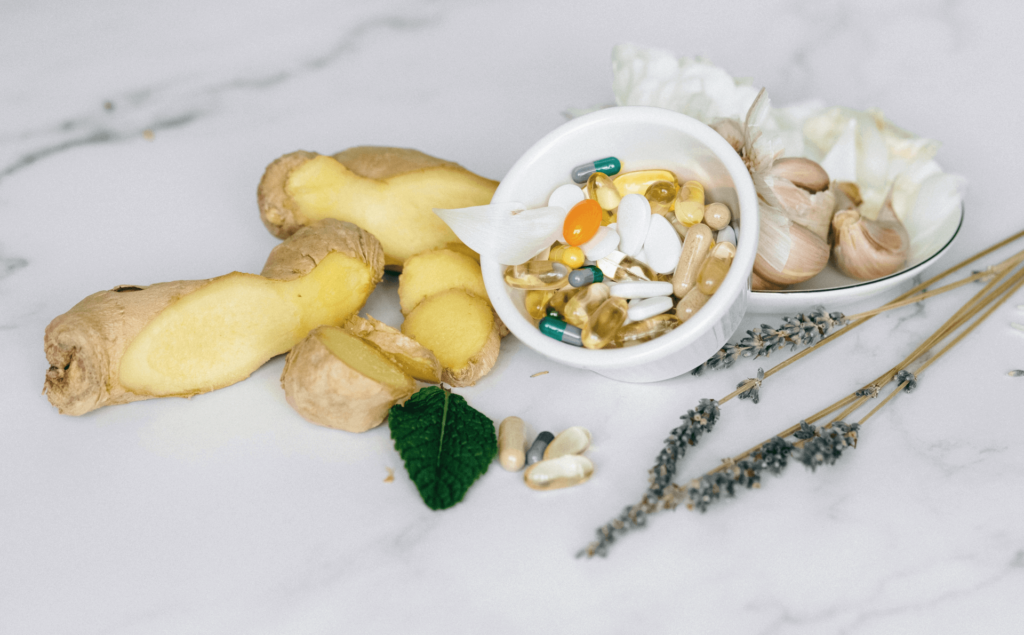 Eine Schale mit Kapseln und Tabletten umgeben von Ingwer Knoblauch und Lavendel